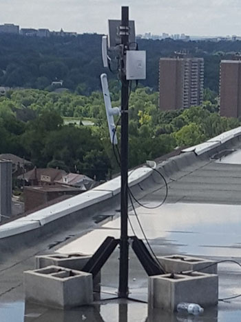 A non-penetrating mount with wireless mesh antennas affixed sitting on an apartment rooftop